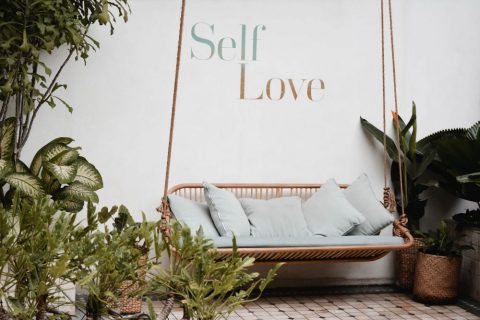 lovely porch area with wicker swing, plants and the words Self Love on the wall